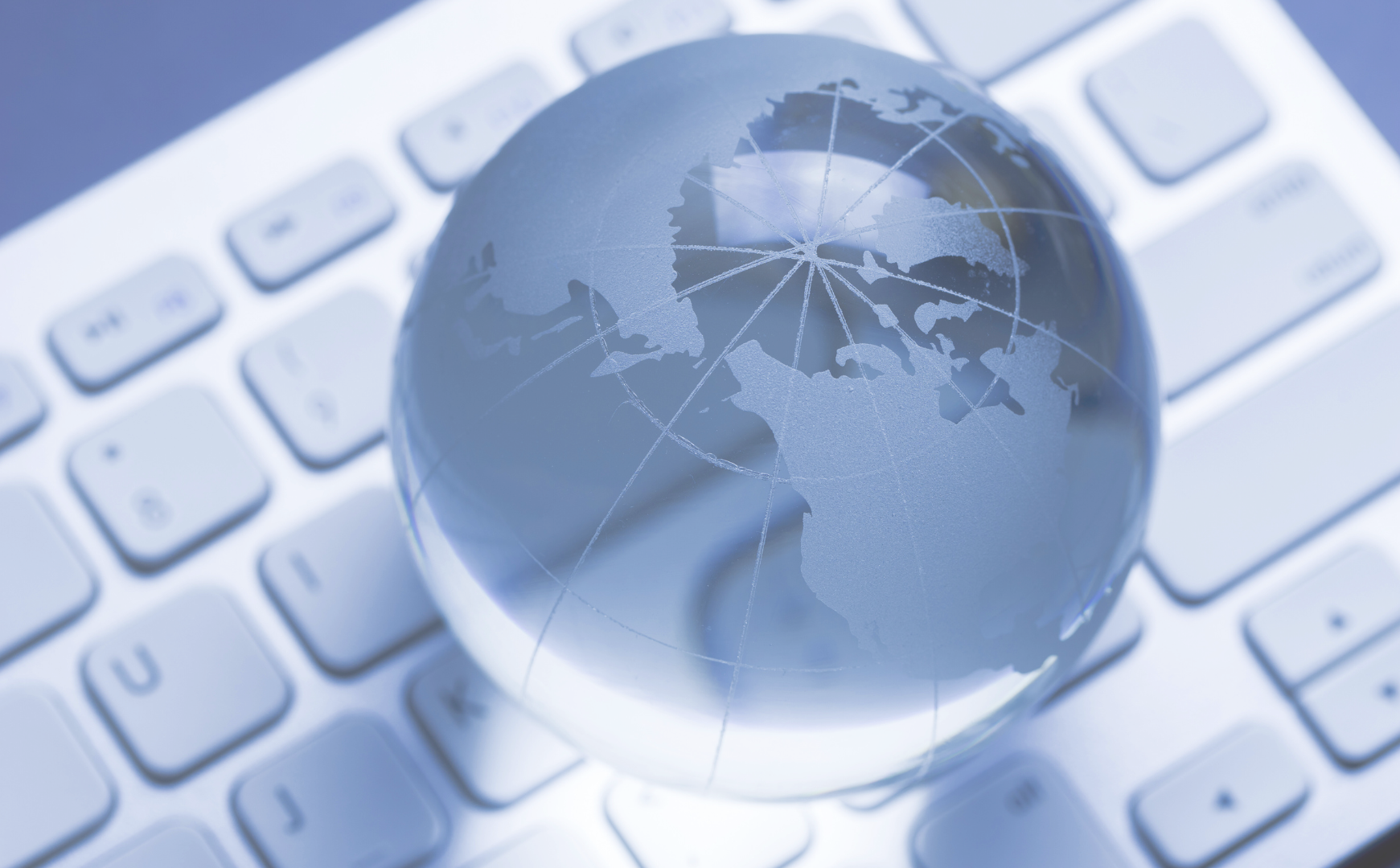 Crystal globe on white keyboard with network connection lines radiating from center, blue-tinted professional image representing global connectivity and strategic business consulting